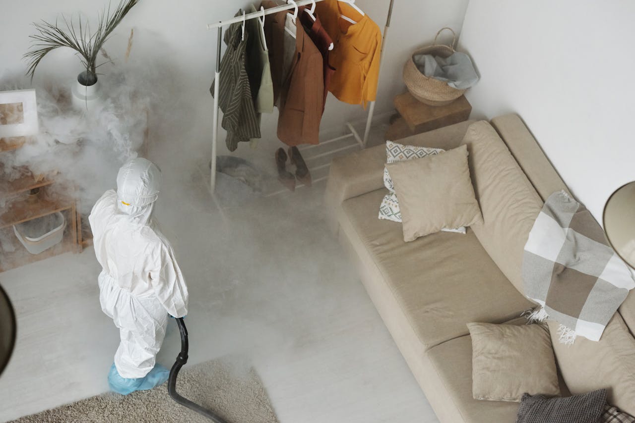 why-choose-us-02 Professional in protective gear sanitizing a modern living room with a fumigation machine.